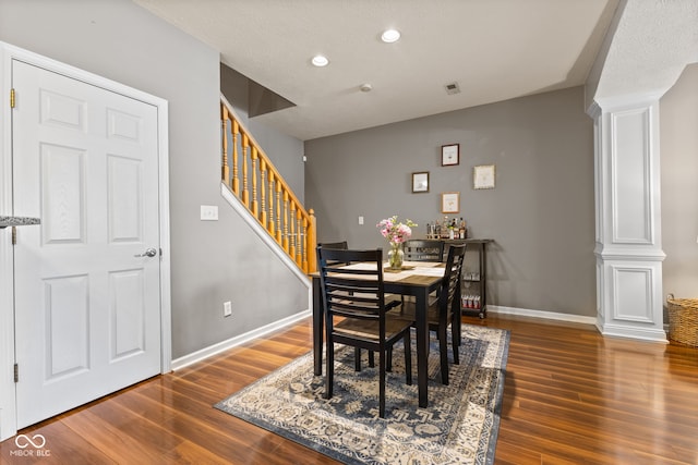 dining area with wood finished floors, visible vents, baseboards, decorative columns, and stairs