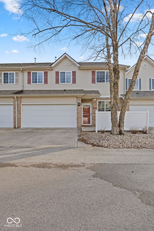 view of property with a garage, brick siding, driveway, and fence