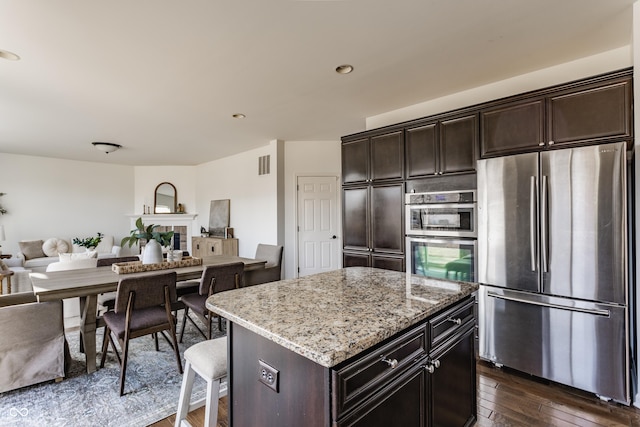 kitchen with visible vents, dark wood-type flooring, open floor plan, stainless steel appliances, and light stone countertops