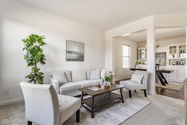 living area with baseboards, crown molding, and carpet