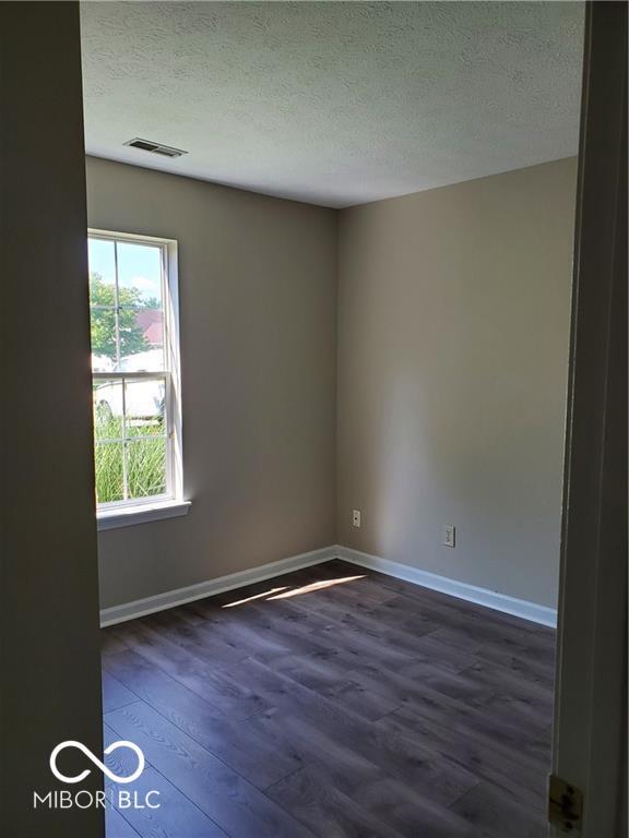 spare room featuring visible vents, dark wood finished floors, a textured ceiling, and baseboards