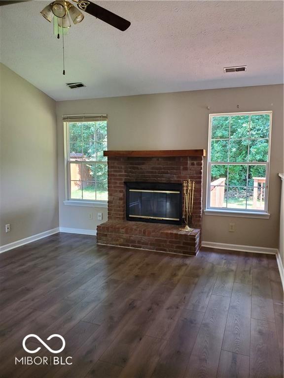 unfurnished living room featuring dark wood-type flooring, a fireplace, visible vents, and a healthy amount of sunlight