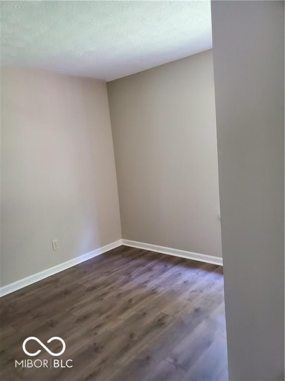 empty room featuring a textured ceiling, baseboards, and dark wood-type flooring