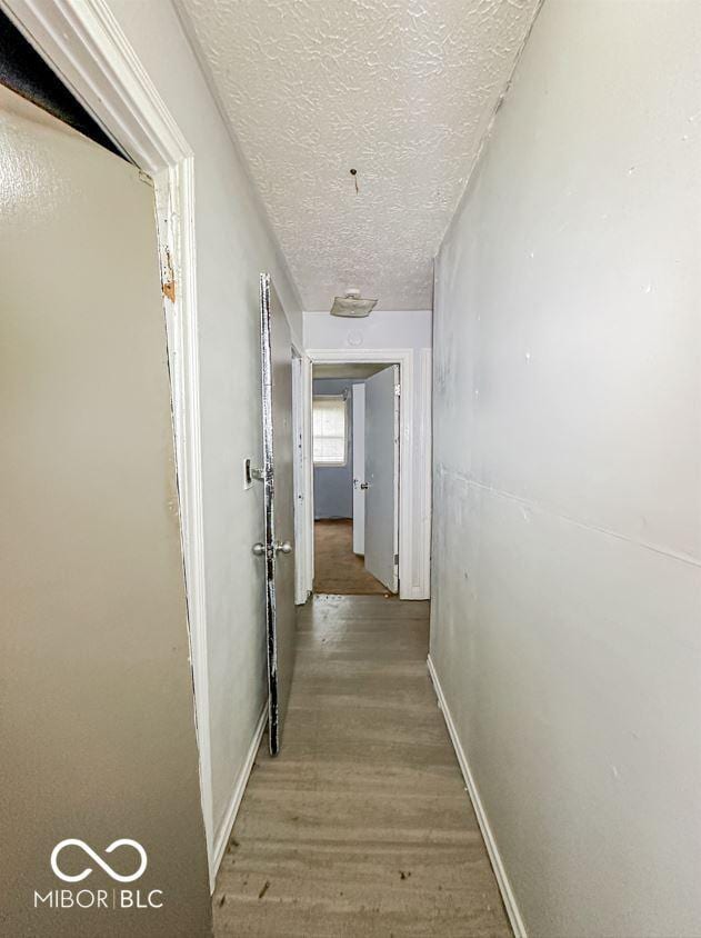 corridor featuring a textured ceiling, wood finished floors, and baseboards