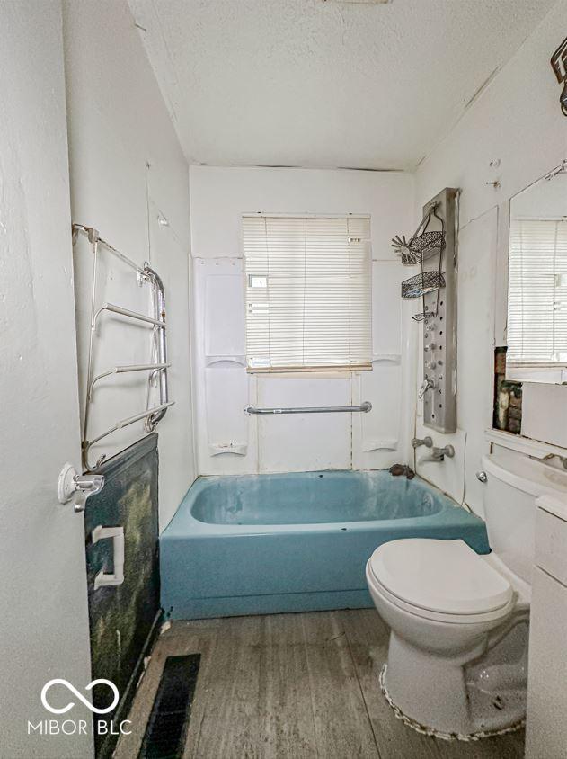 full bath with a textured ceiling, bathtub / shower combination, wood finished floors, and toilet