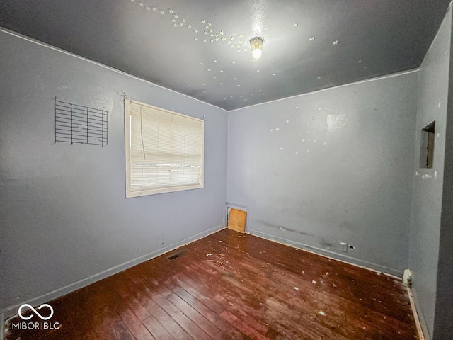 empty room featuring wood-type flooring, visible vents, and baseboards