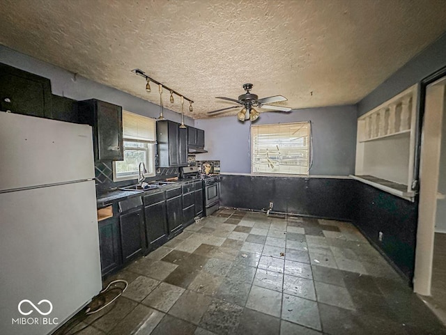 kitchen with freestanding refrigerator, stainless steel range with gas stovetop, a sink, a textured ceiling, and dark cabinetry