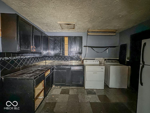 kitchen with dark countertops, freestanding refrigerator, a textured ceiling, separate washer and dryer, and backsplash