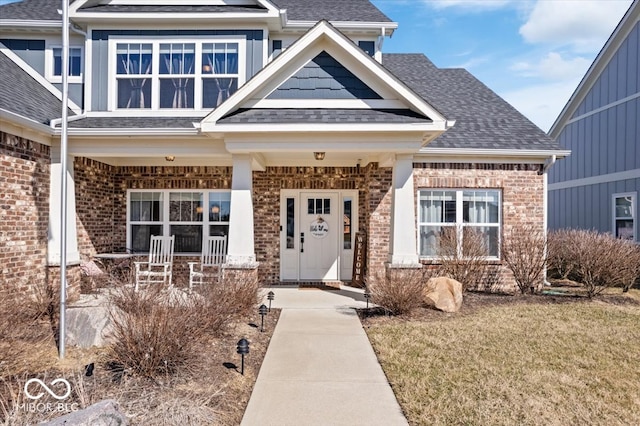 view of exterior entry featuring brick siding, covered porch, and a shingled roof