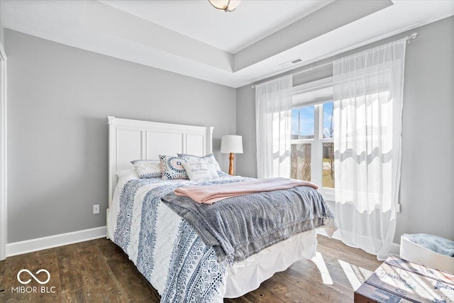 bedroom featuring a tray ceiling, baseboards, visible vents, and wood finished floors