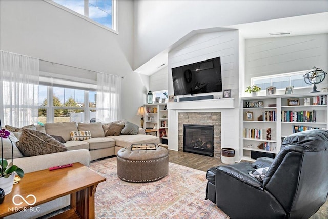 living room with a glass covered fireplace, a towering ceiling, visible vents, and wood finished floors