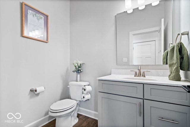 half bath with vanity, toilet, wood finished floors, and baseboards