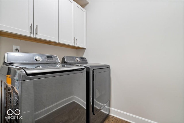 clothes washing area with washer and clothes dryer, cabinet space, baseboards, and wood finished floors