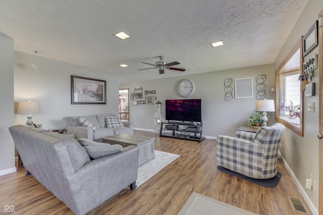 living room with visible vents, baseboards, wood finished floors, a textured ceiling, and a ceiling fan