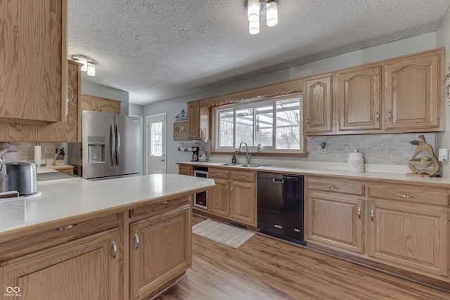 kitchen featuring light wood-type flooring, stainless steel refrigerator with ice dispenser, a sink, black dishwasher, and light countertops