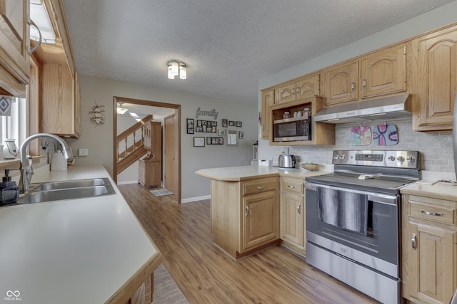 kitchen featuring under cabinet range hood, light countertops, appliances with stainless steel finishes, a peninsula, and a sink