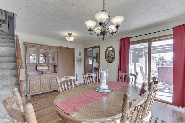 dining space with a textured ceiling, an inviting chandelier, light wood-style flooring, and stairs