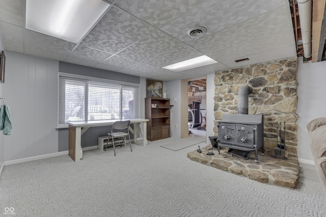 home office with a wood stove, a paneled ceiling, visible vents, and carpet floors