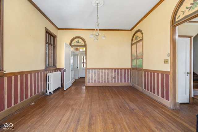 spare room featuring wood finished floors, wainscoting, radiator heating unit, and ornamental molding