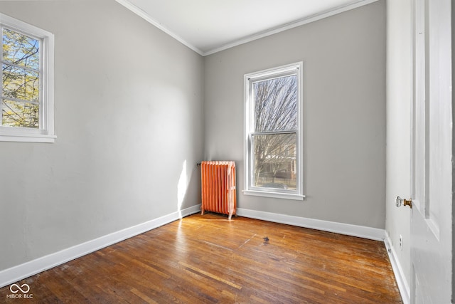 empty room with ornamental molding, radiator heating unit, baseboards, and wood-type flooring