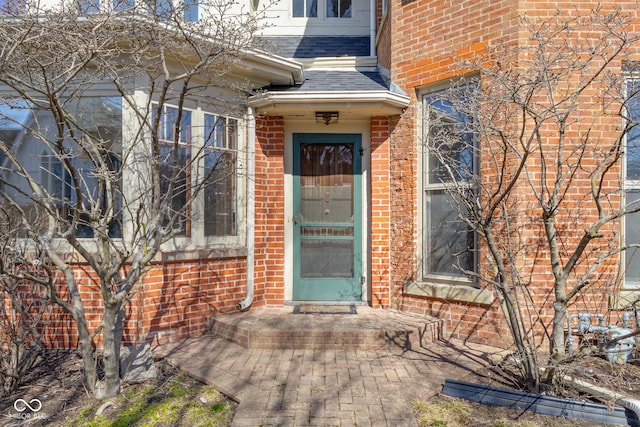 entrance to property featuring brick siding and roof with shingles