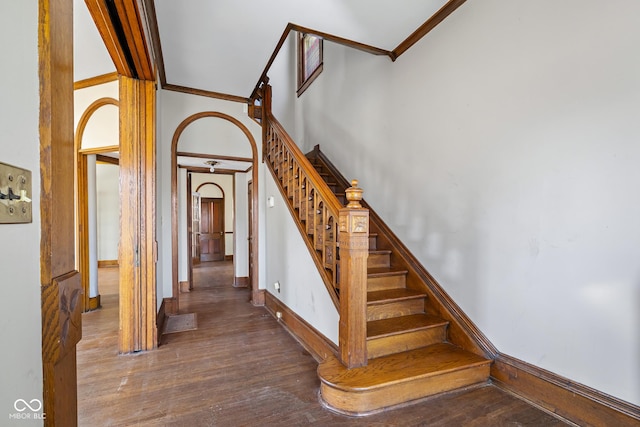 stairway featuring baseboards, wood finished floors, arched walkways, and ornamental molding