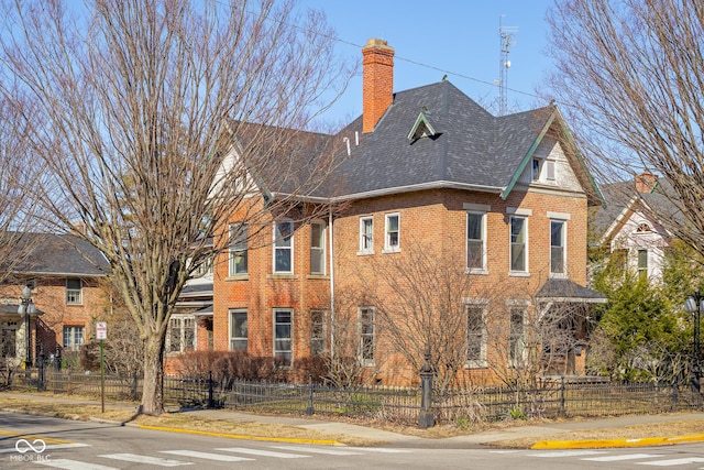 view of front of house featuring a fenced front yard, brick siding, roof with shingles, and a chimney