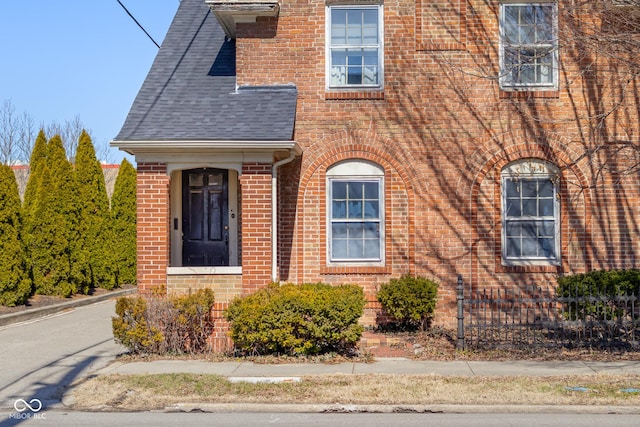 doorway to property with brick siding and roof with shingles