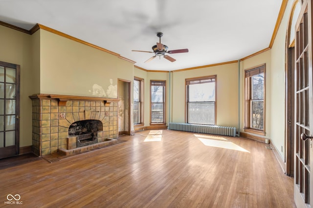 unfurnished living room with radiator, wood finished floors, baseboards, ornamental molding, and a tile fireplace