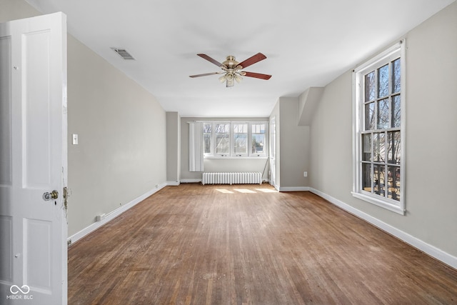 unfurnished living room featuring visible vents, wood finished floors, radiator, baseboards, and ceiling fan