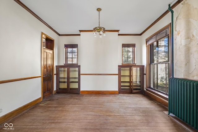 empty room featuring baseboards, wood finished floors, radiator heating unit, and ornamental molding