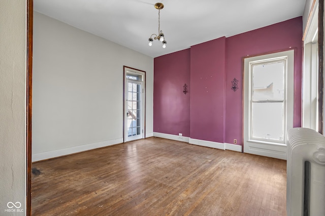 spare room with baseboards, a notable chandelier, wood finished floors, and radiator heating unit