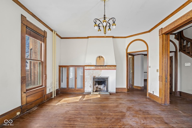 unfurnished living room featuring a large fireplace, a notable chandelier, wood finished floors, and crown molding