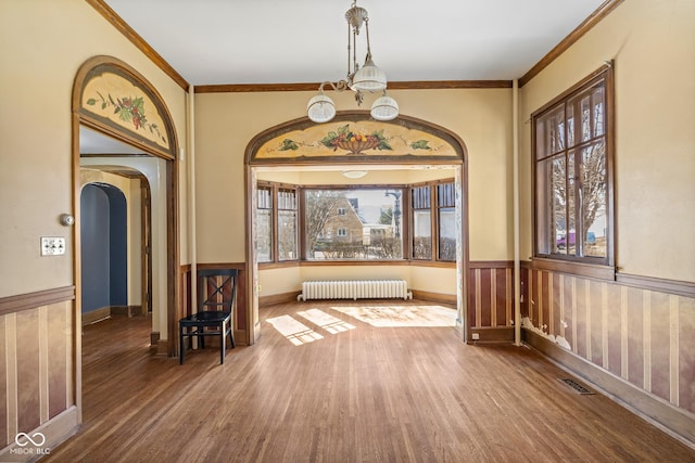 foyer featuring visible vents, a wainscoted wall, radiator heating unit, wood finished floors, and arched walkways