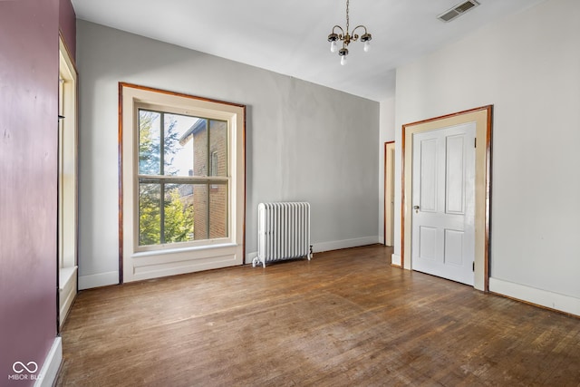 empty room with visible vents, wood-type flooring, radiator, an inviting chandelier, and baseboards