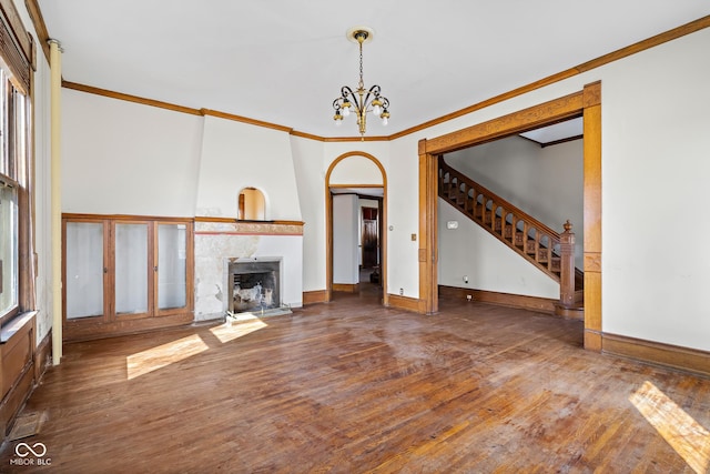 unfurnished living room with stairs, wood-type flooring, crown molding, a notable chandelier, and a large fireplace