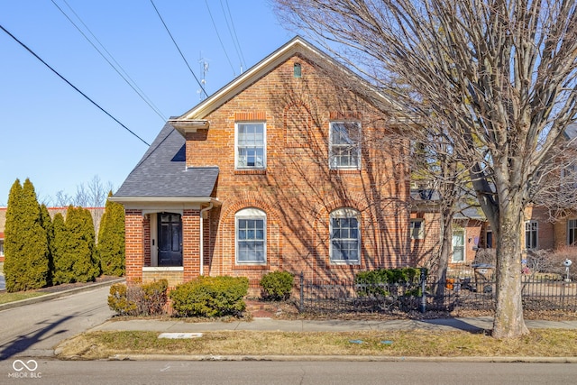 view of front of property featuring brick siding, roof with shingles, and fence