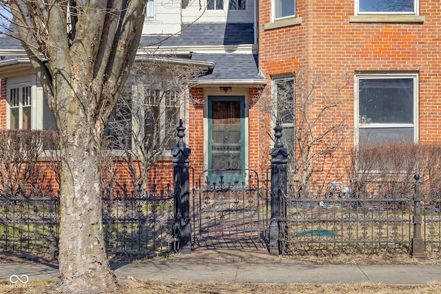 view of exterior entry featuring fence, brick siding, and a shingled roof