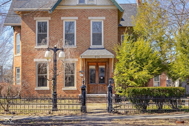 view of front of home featuring brick siding, entry steps, a fenced front yard, and roof with shingles