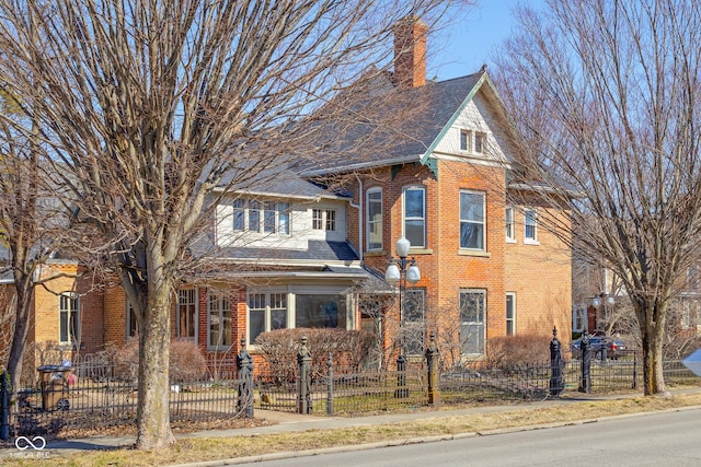 view of front of property featuring brick siding, a chimney, and a fenced front yard