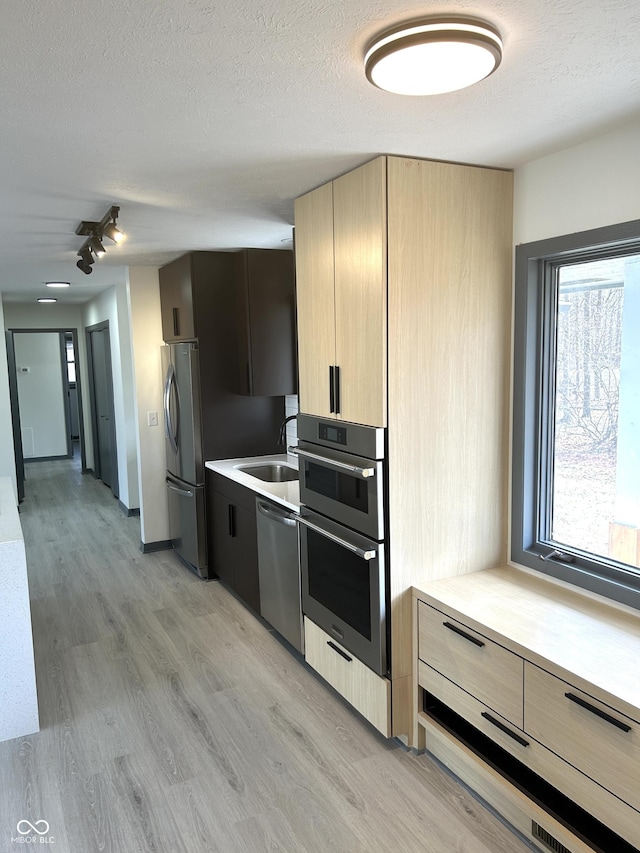 kitchen with light countertops, light wood finished floors, modern cabinets, and appliances with stainless steel finishes