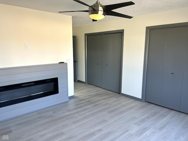 unfurnished living room featuring a glass covered fireplace, ceiling fan, a textured ceiling, and light wood-style floors