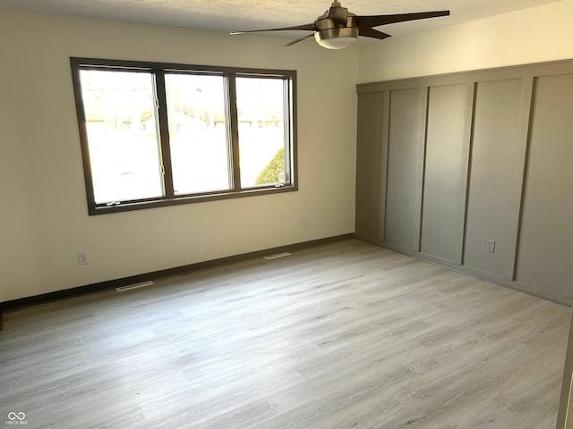 unfurnished bedroom featuring ceiling fan, light wood-style floors, visible vents, and baseboards