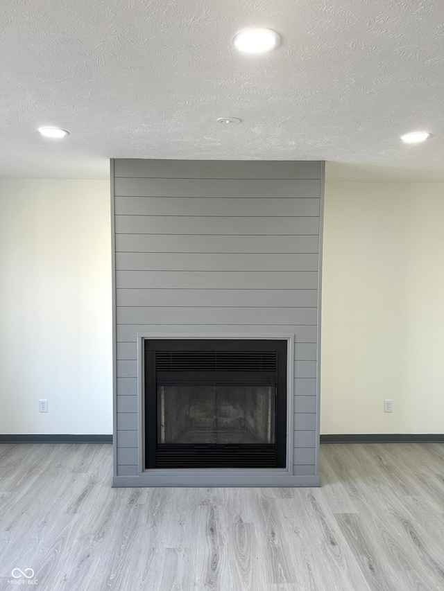 room details with a textured ceiling, wood finished floors, baseboards, and a large fireplace