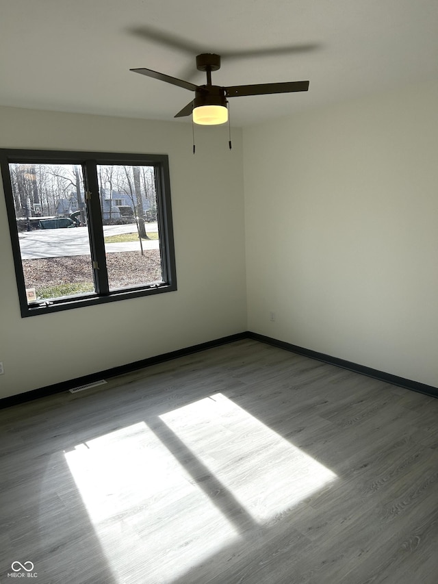 spare room featuring visible vents, baseboards, ceiling fan, and wood finished floors