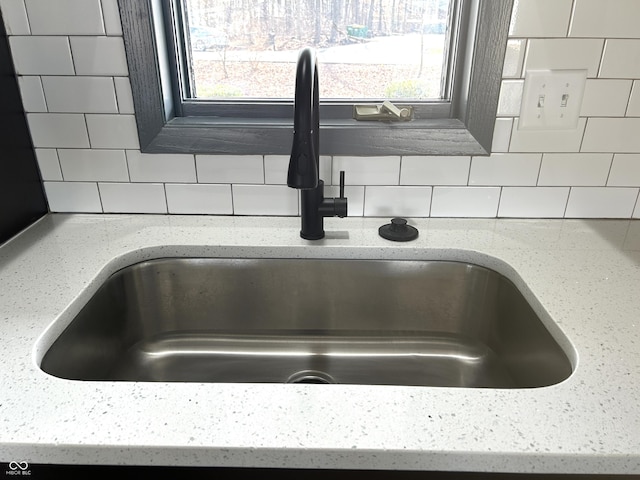 details featuring light stone counters, decorative backsplash, and a sink