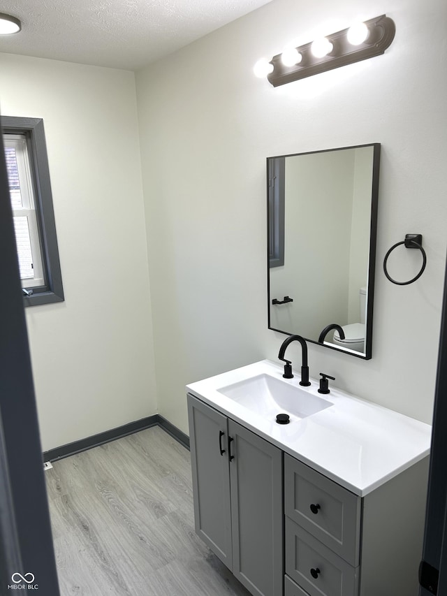 half bath featuring toilet, a textured ceiling, wood finished floors, baseboards, and vanity