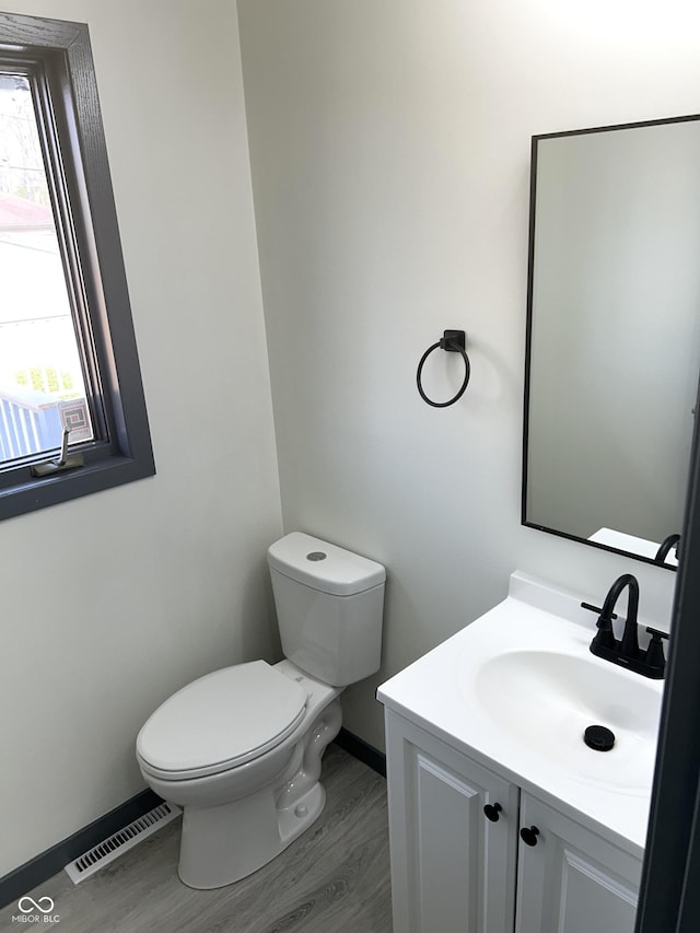 bathroom featuring visible vents, baseboards, toilet, wood finished floors, and vanity