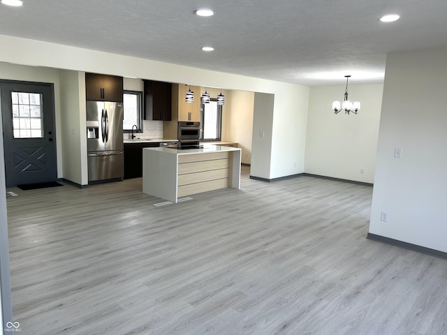 kitchen with light wood-type flooring, a notable chandelier, a center island, stainless steel appliances, and light countertops