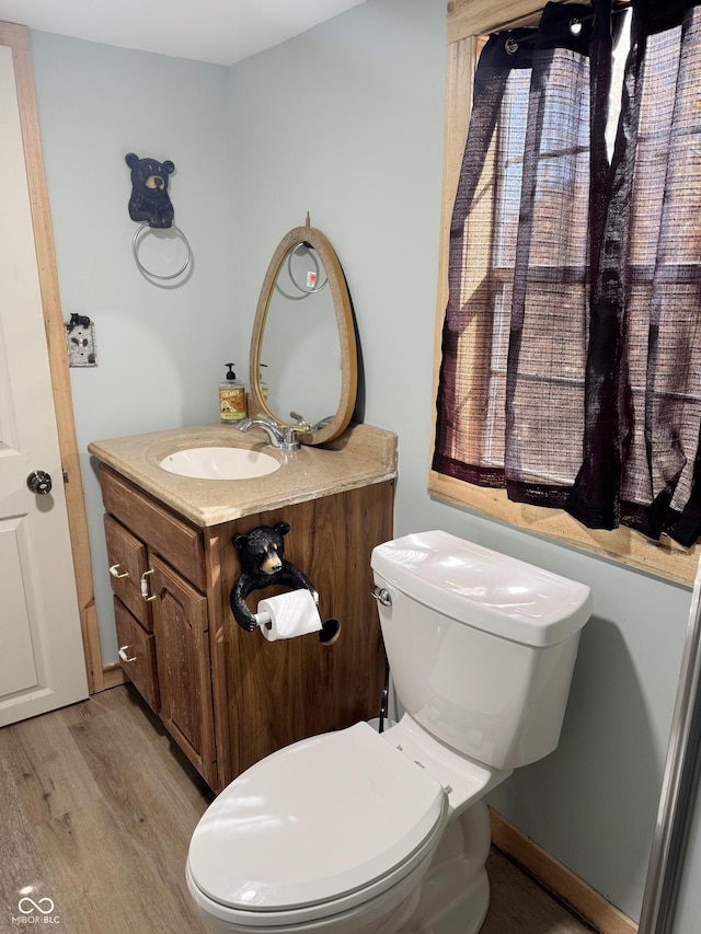 half bath with toilet, wood finished floors, and vanity